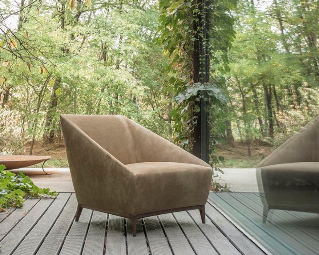 Zoe Armchair by Alivar in brown leather, emphasizing its geometric form and slender wooden legs, set against a natural backdrop